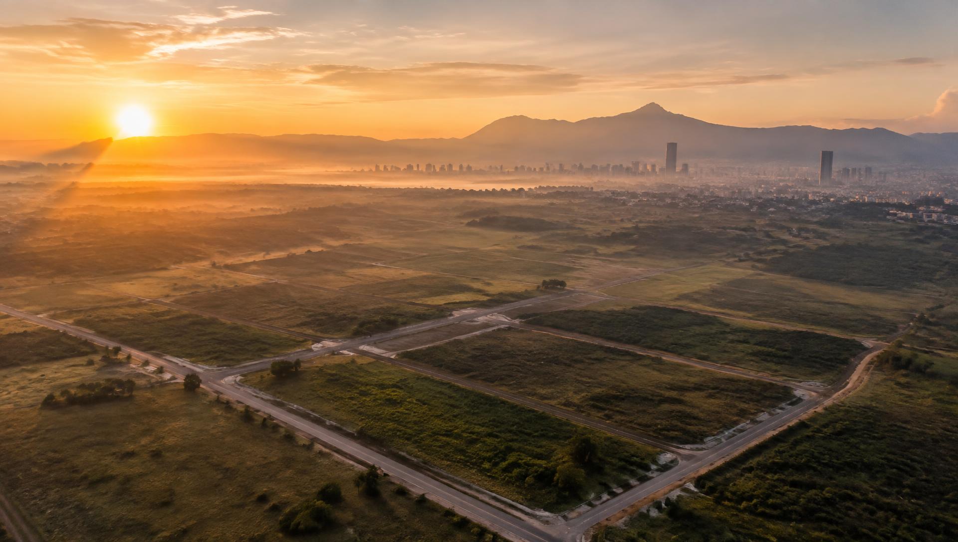 Vista aérea de terrenos al amanecer frente a una ciudad